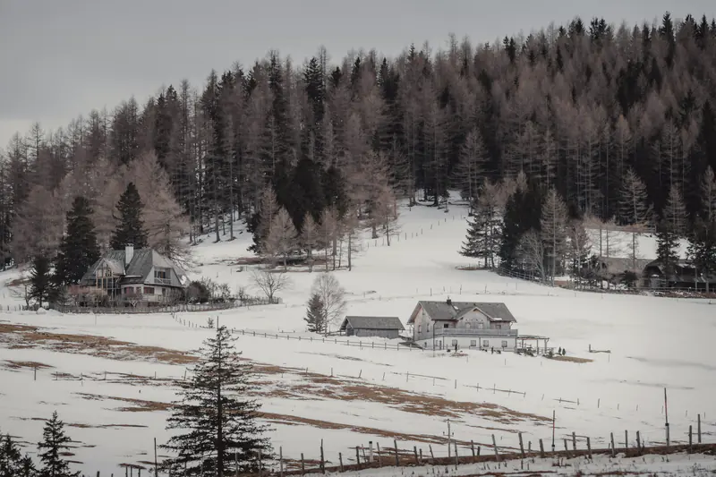 Snowy foothills valley with houses below a forested ridge