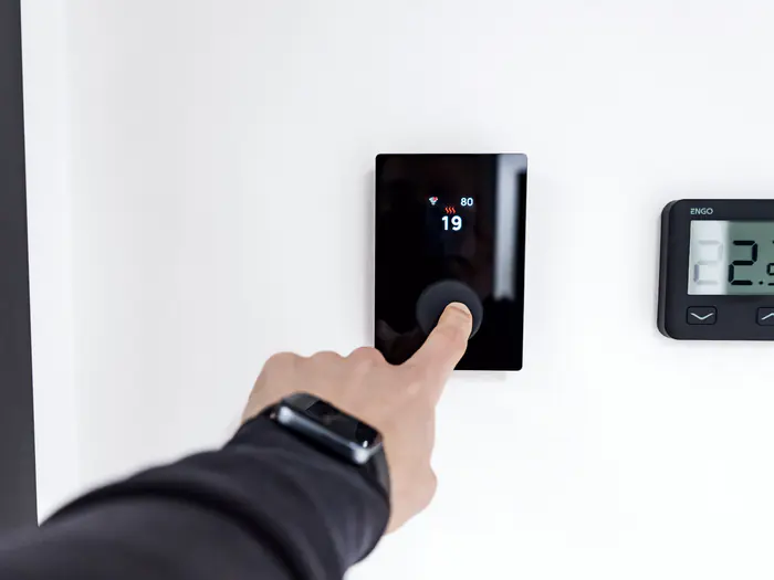 Hand adjusting a wall thermostat next to a digital temperature display